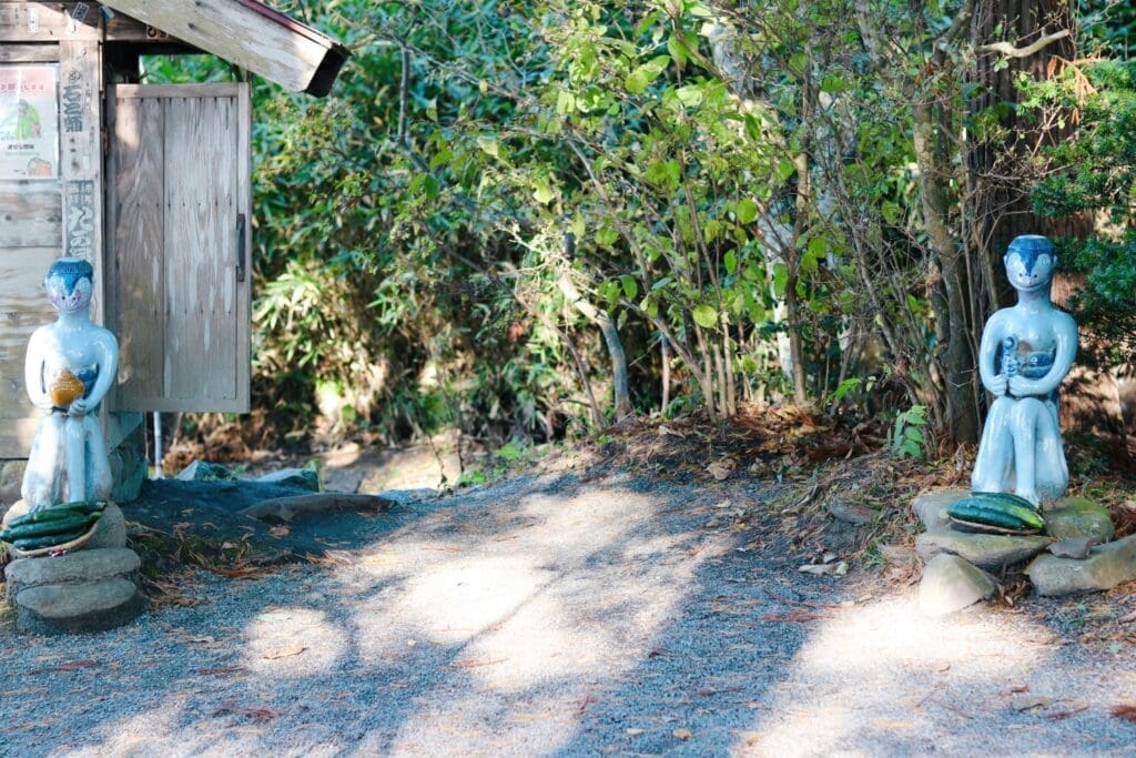 Kappa statues guarding small shrine by Kappabuchi. Cucumbers are offered at their feet.